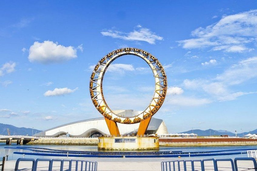A Ferris wheel with a circular structure, a large white building, and a clear blue sky. 4