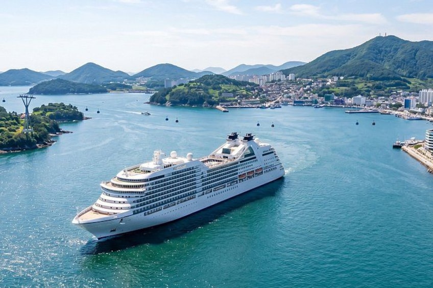 A large cruise ship sailing in a harbor with mountains and a city in the background. 1