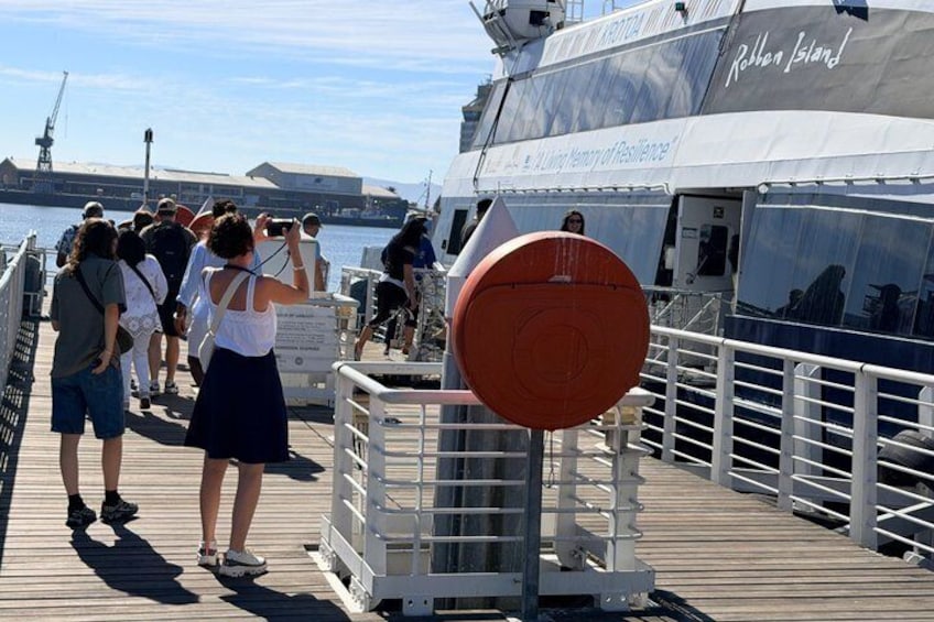 A pier with people walking and taking photos, a large ship with 'Rothen Island' written on it, and a clear sky. 2