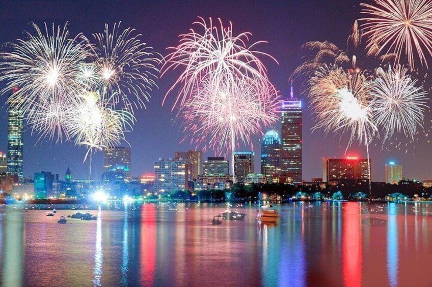 A city skyline with fireworks over a body of water reflecting city lights. 1