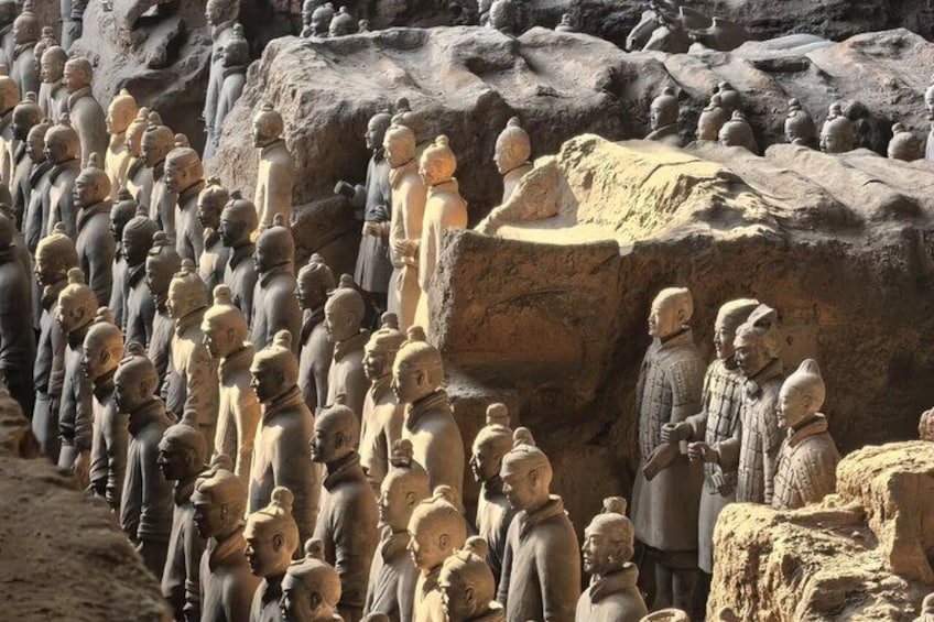 A row of stone statues, some standing and some seated, on a rocky terrain. 4