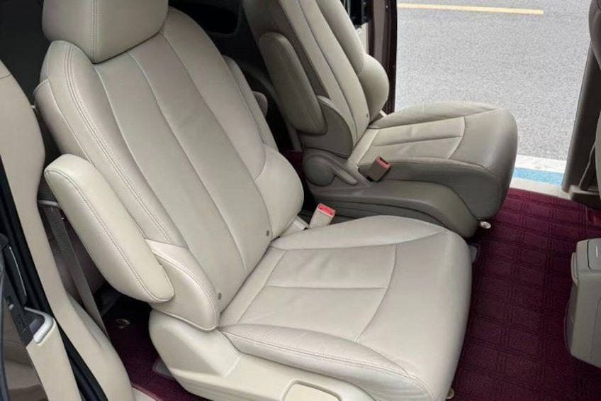 A car interior with beige leather seats and a maroon floor mat. 2