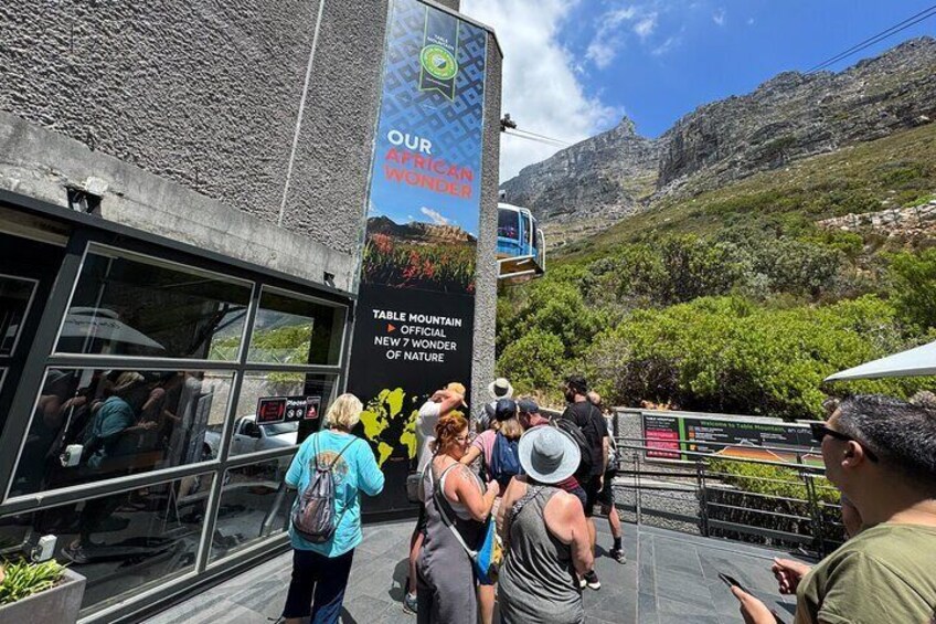 A group of people at a tourist site with a mountain backdrop and a cable car in the distance. 1