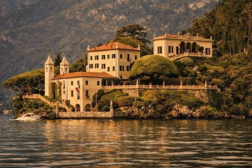 A lakeside villa with a tower, surrounded by lush greenery and mountains. 2