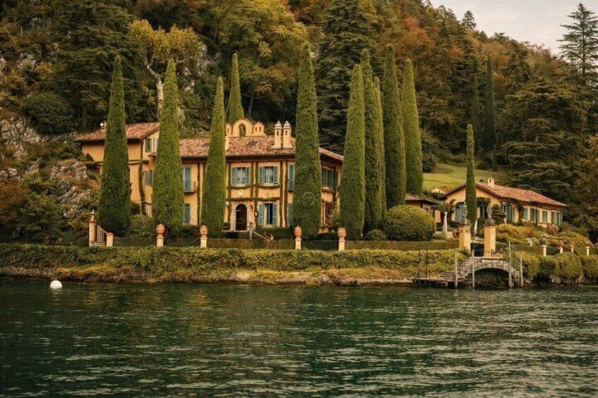 A lakeside villa with a bridge, surrounded by tall cypress trees and a mountainous backdrop. 3