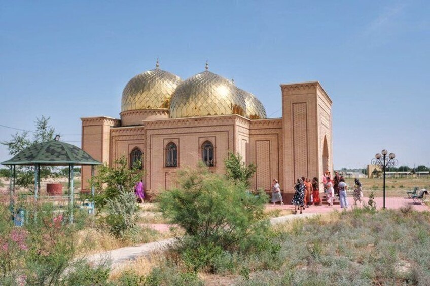 A large building with golden domes, surrounded by greenery and a few people. 2