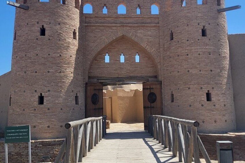 A medieval castle entrance with a wooden walkway leading to a large arched doorway. 1