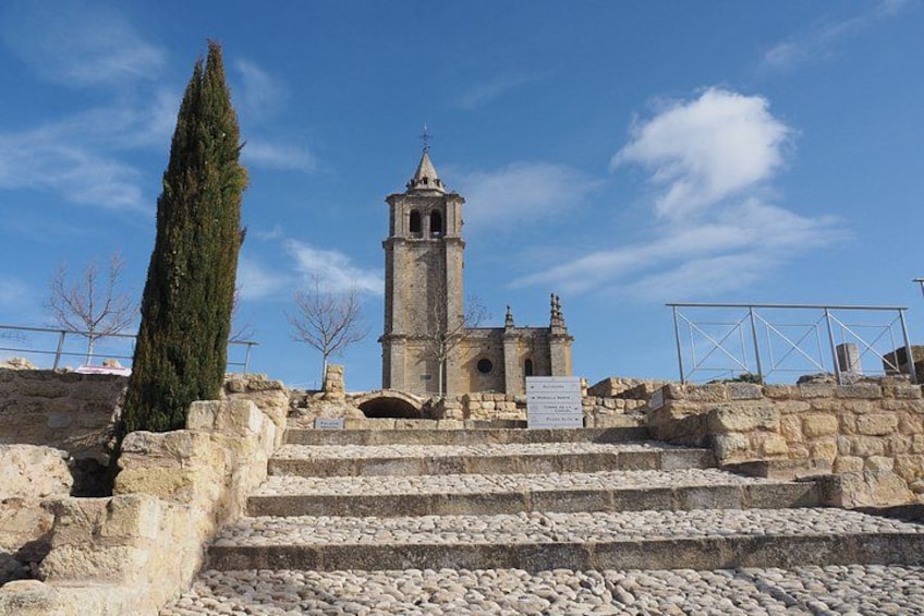 A historical stone staircase leading to a bell tower with a cross on top, surrounded by stone walls and a clear sky. 4