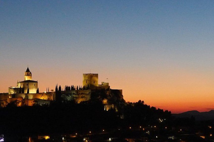 A historic castle with a prominent tower and a fortified wall, set against a twilight sky. 5