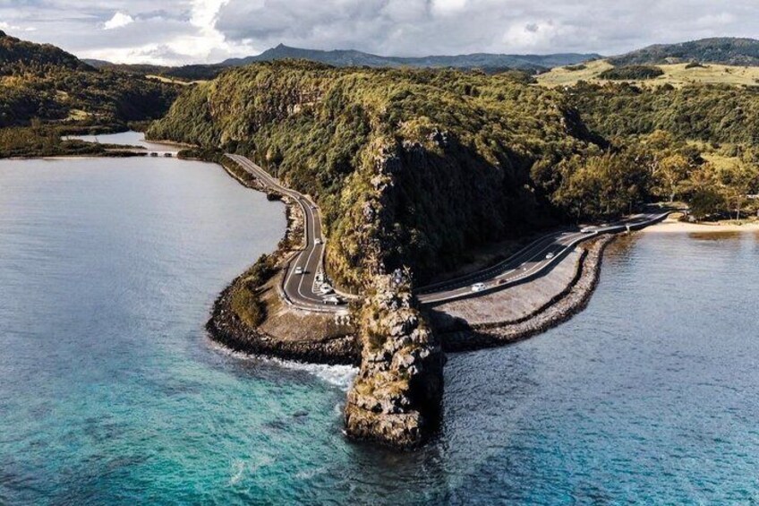 A coastal road curving around a rocky island with clear blue waters. 1