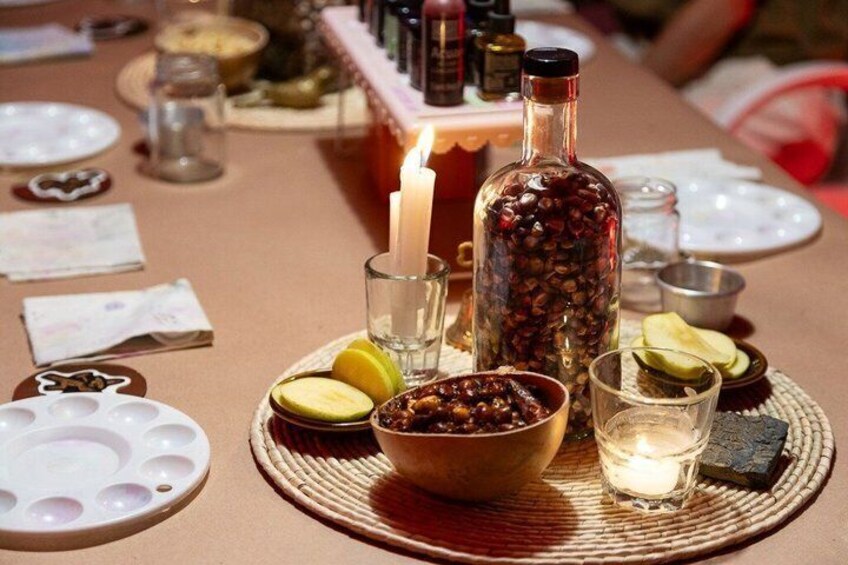 A table set with a candle, a bottle of coffee beans, a bowl of nuts, and a plate with cut lemons. 3