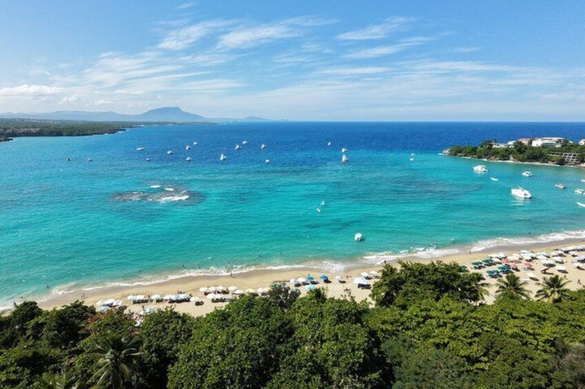 A beach with clear turquoise waters, boats, and umbrellas. 1