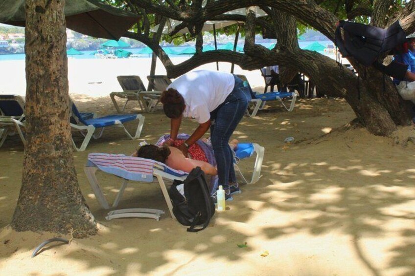 A person attending to someone lying on a beach chair, with beach umbrellas and lounge chairs in the background. 5