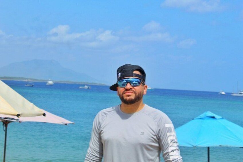 A person standing by a beach with umbrellas and boats in the background. 4