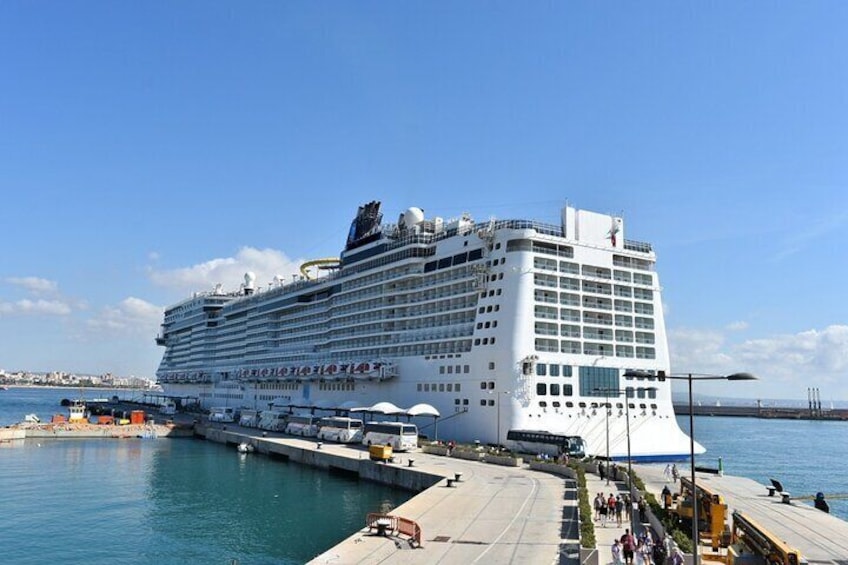 A large cruise ship docked at a port with a clear sky and calm sea. 1