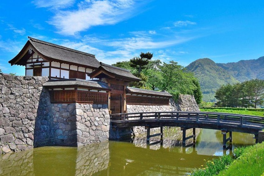 A traditional Japanese building with a stone base, a wooden structure, and a bridge over a pond. 1