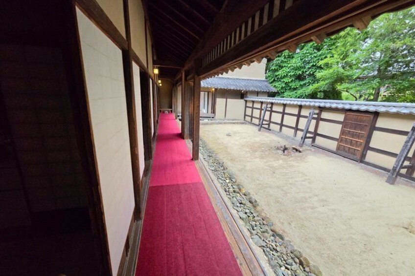 A traditional Japanese corridor with a red carpet, wooden walls, and a gravel path. 4