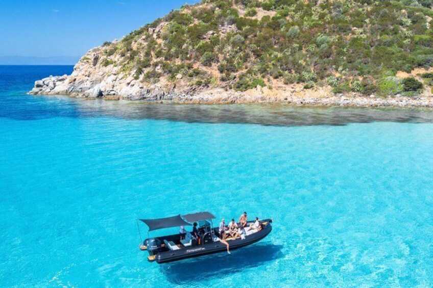 A boat on clear turquoise water with a rocky coastline and sparse vegetation. 2