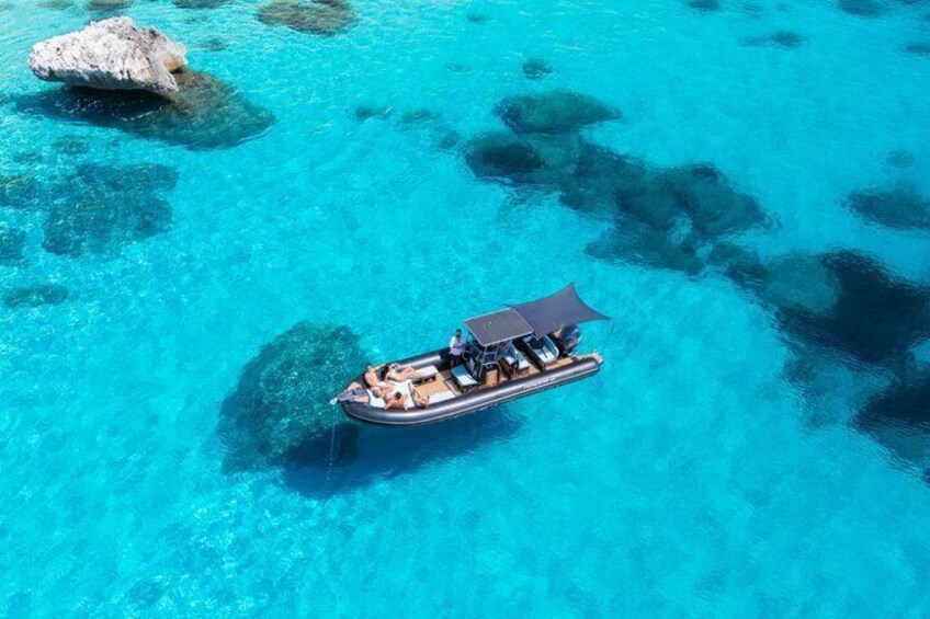 A boat with a canopy on clear turquoise water, surrounded by rocks. 1