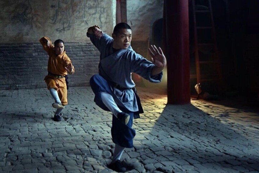 Two individuals practicing martial arts in a dimly lit room with stone flooring and wooden beams. 2