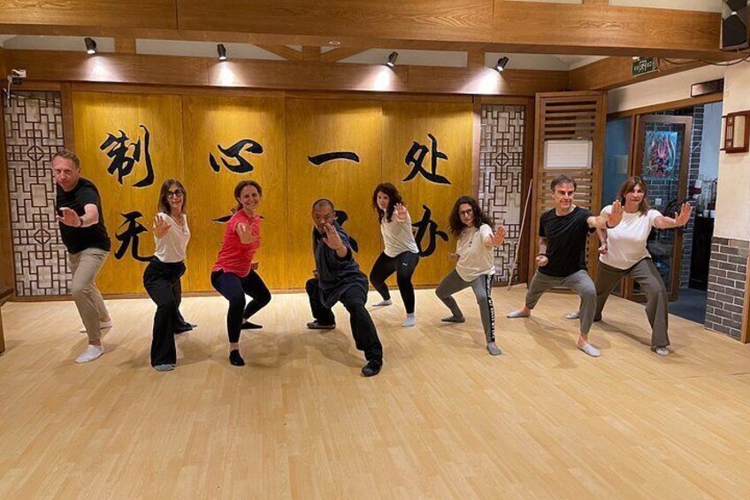 A group of people in a dance studio with wooden floors and walls adorned with Asian calligraphy. 4