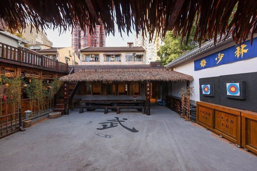 A traditional courtyard with a thatched roof, wooden benches, and a wall with Chinese characters. 5