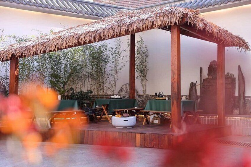 A traditional thatched-roof pavilion with tables and chairs, surrounded by bamboo plants. 2