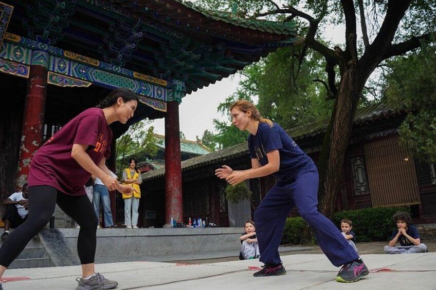 Two people performing a martial arts demonstration in front of a traditional Chinese building. 1