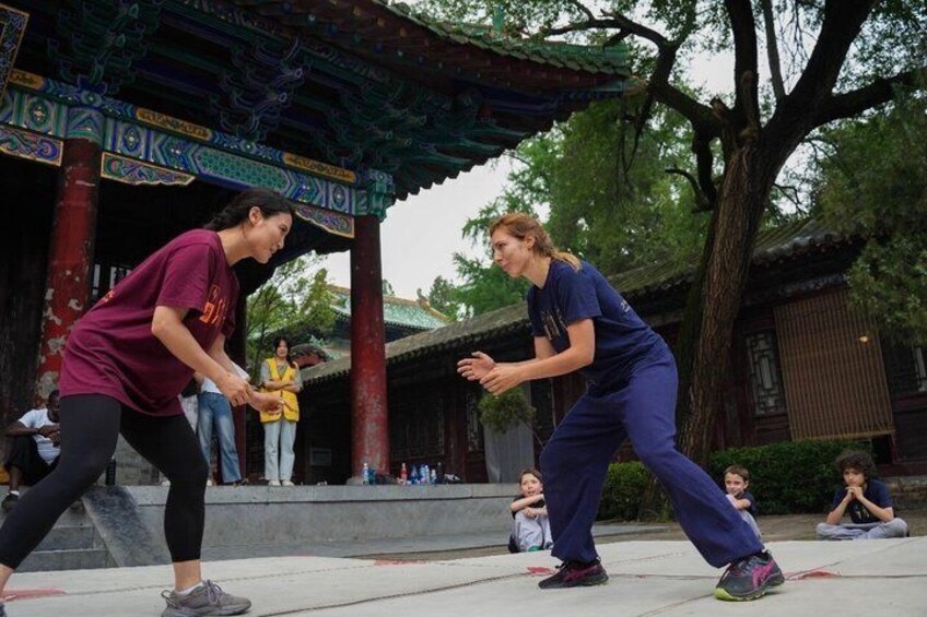 Two people performing a martial arts demonstration in front of a traditional Chinese pavilion. 1