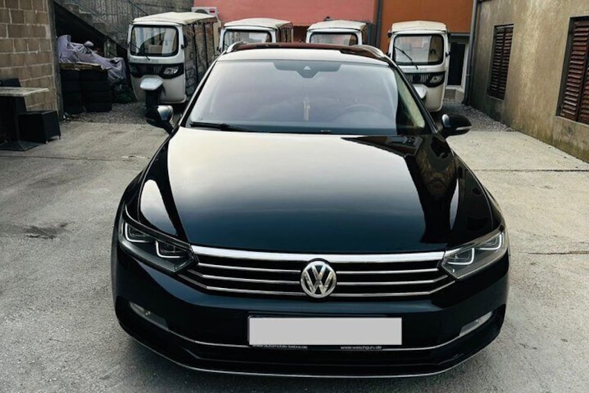 A black Volkswagen car parked in an outdoor area with other vehicles and buildings in the background. 5