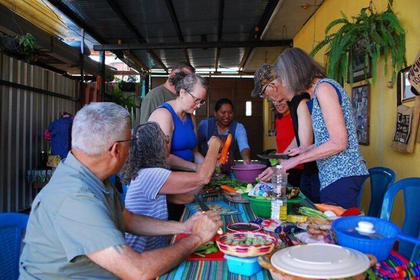 A group of people preparing food at a table with various vegetables and dishes. 2
