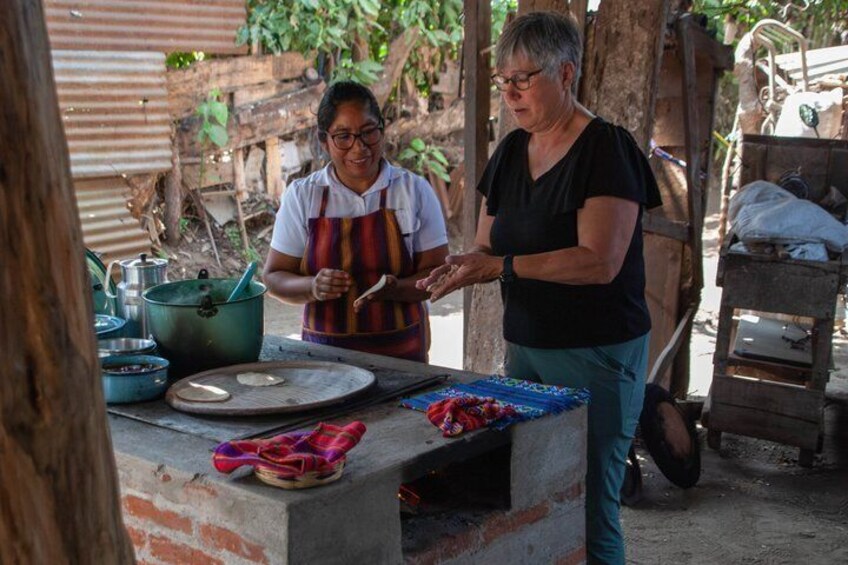 Two women cooking outdoors with pots and pans on a brick stove. 1