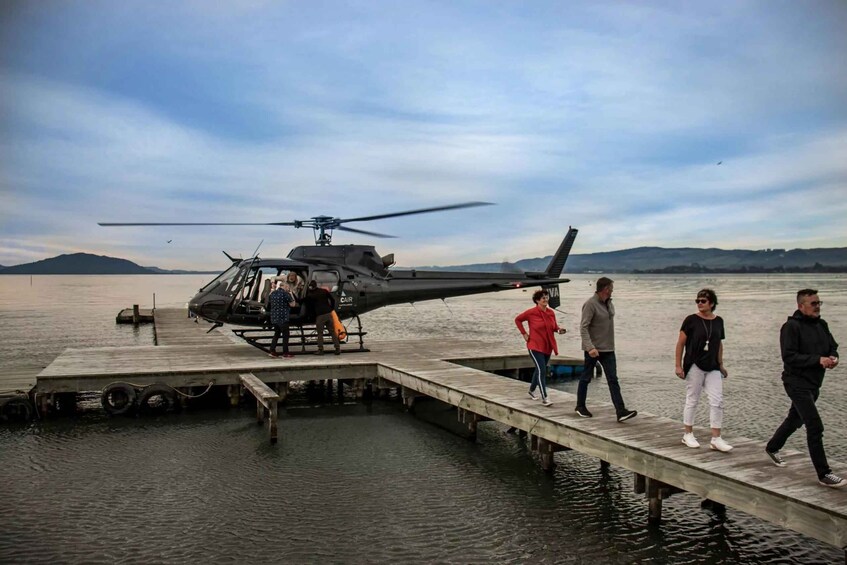 A helicopter parked on a dock with people walking around it. 1