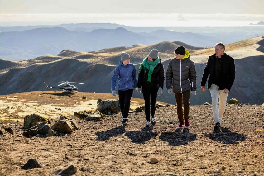 Four people walking on a rocky mountain path with a helicopter in the background. 3