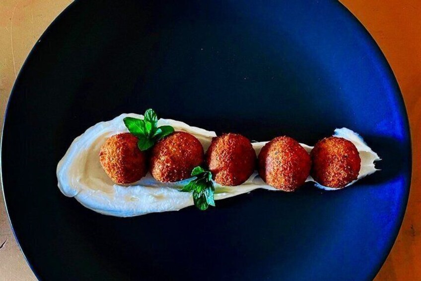A plate with five round, golden-brown fried balls on a white sauce, garnished with green leaves. 5