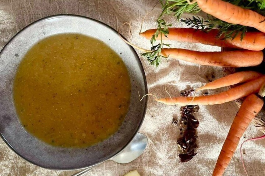 A bowl of soup with carrots and herbs on a cloth. 1