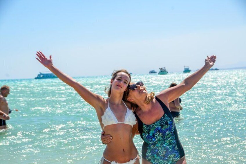 Two people embracing in the ocean with a clear sky and boats in the background. 5