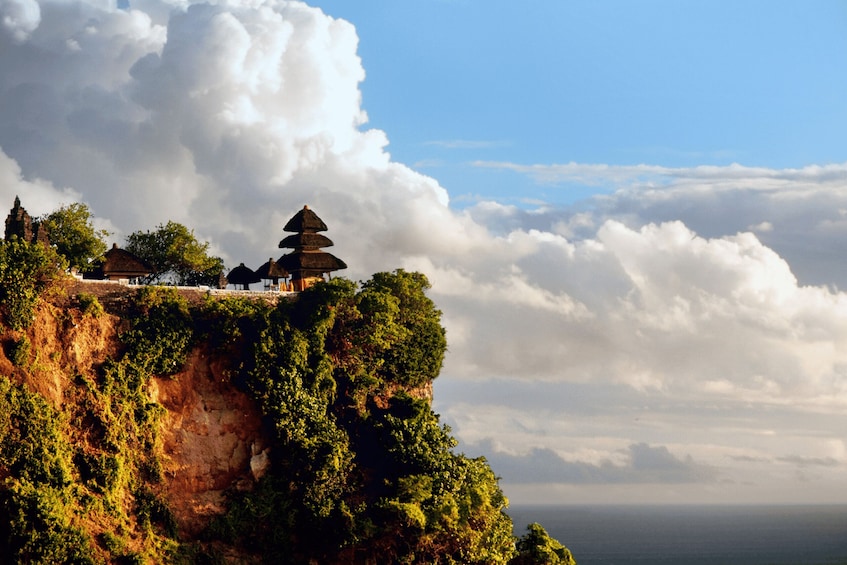 A temple on a cliff with lush greenery and a view of the ocean. 2