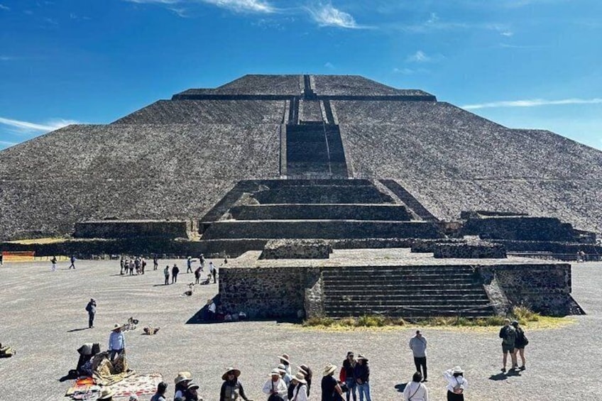 A large pyramid with a staircase leading to the top, surrounded by a paved area with people walking around. 3