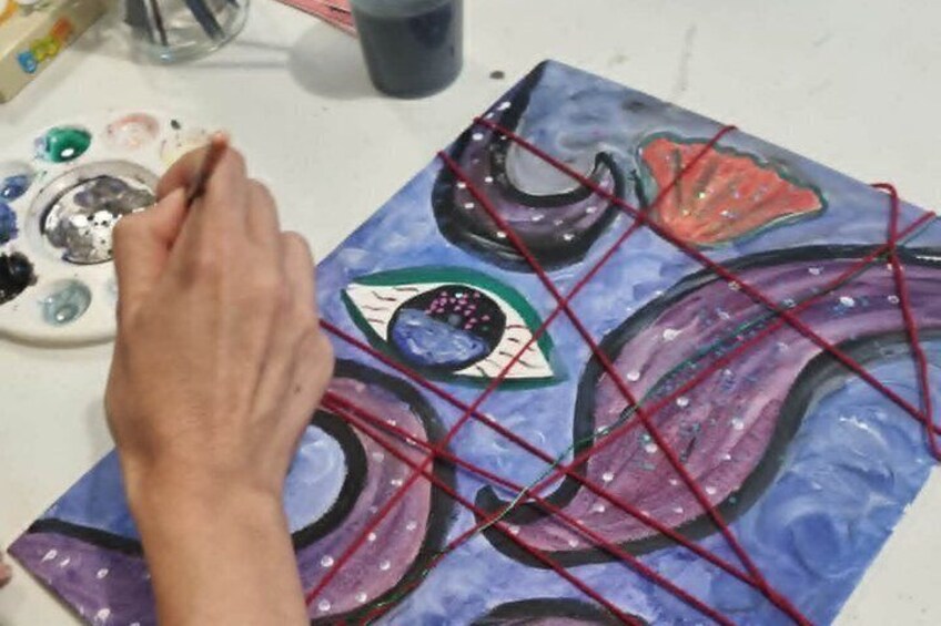 A hand painting a canvas with abstract designs and red lines. 1