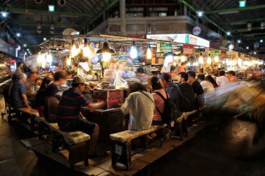 A bustling indoor market with people seated at tables, illuminated by hanging lights. 5