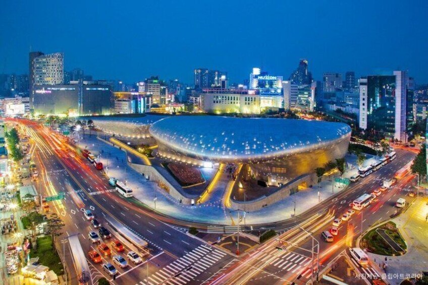A modern stadium with a unique curved roof, surrounded by a busy urban area with multiple roads and buildings. 3