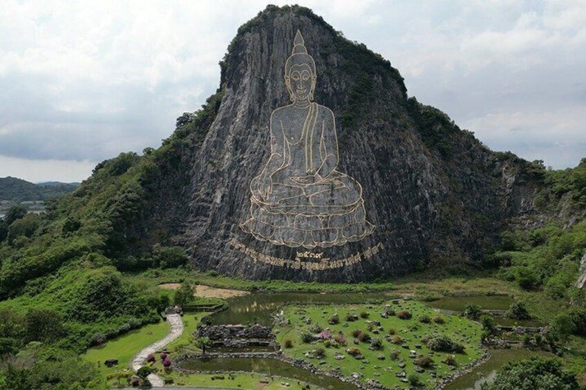 A large rock formation with a Buddha statue carved into it, surrounded by lush greenery and a small pond. 5