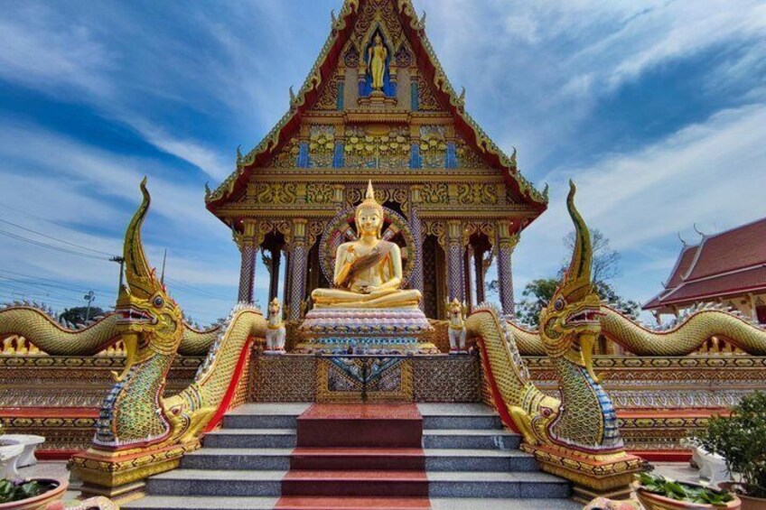 A golden Buddha statue in front of a traditional Thai temple with ornate decorations and two dragon statues. 4
