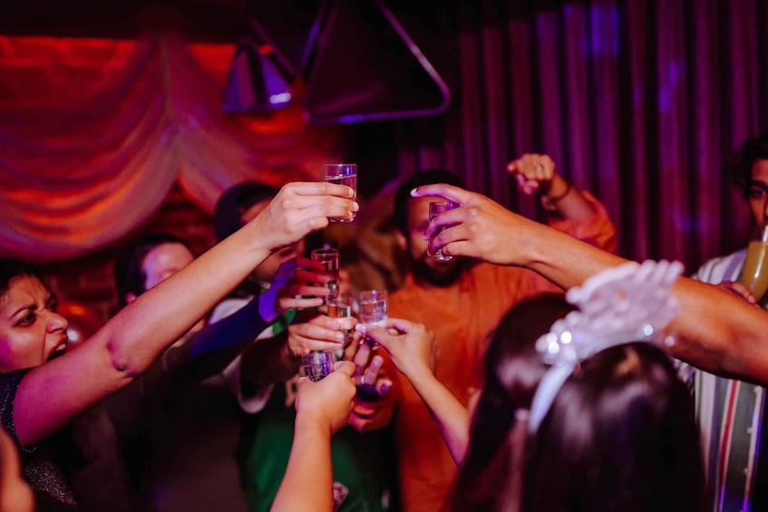 A group of people toasting with drinks in a dimly lit venue with draped curtains. 1