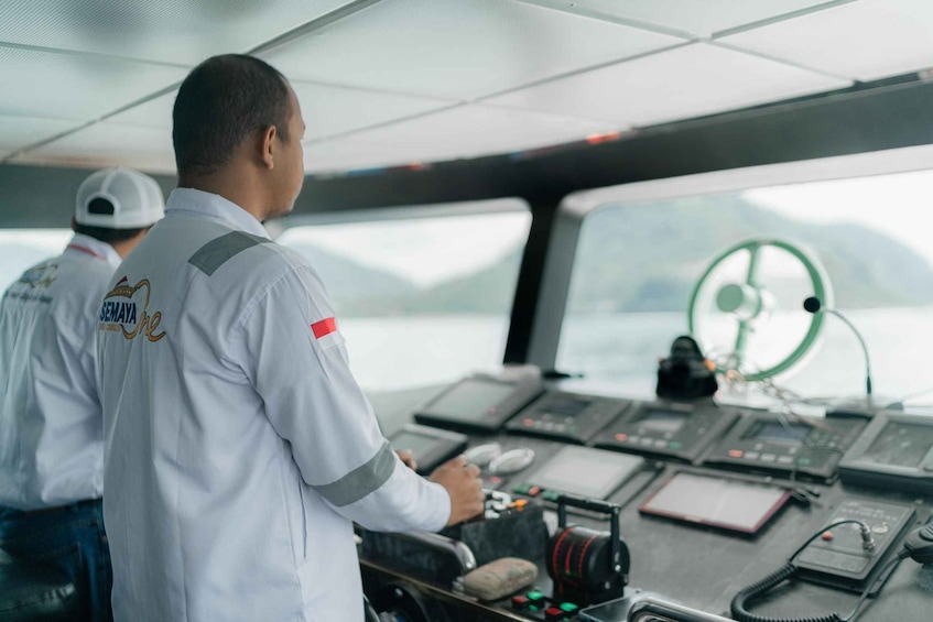 Two individuals in a control room with various instruments and a steering wheel. 5