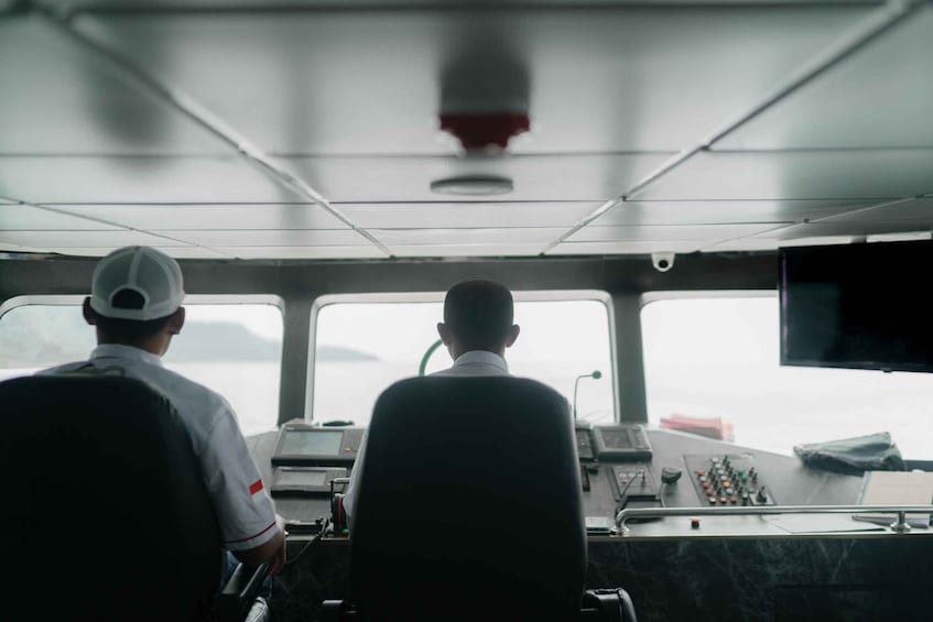 Two individuals in a control room with a view of the sea through windows. 2