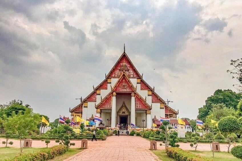 A traditional Thai temple with a central entrance, surrounded by well-maintained gardens and multiple flags. 3