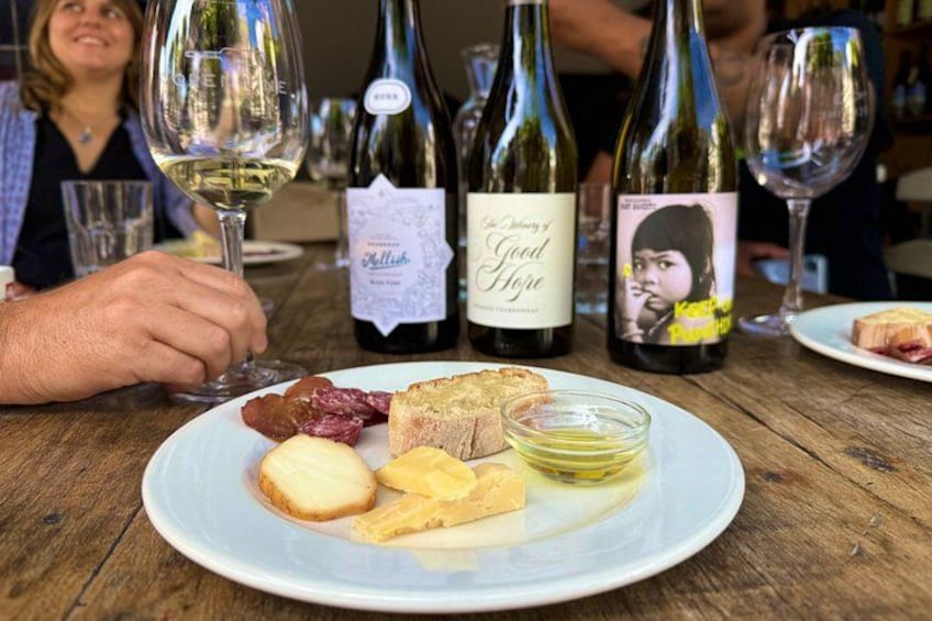 A wooden table with a plate of food, wine bottles, and glasses. 3