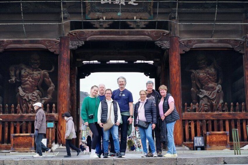 A group of people standing in front of a traditional wooden gate with intricate carvings. 3